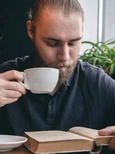Bărbat care bea ceai și citește o carte la o cafenea