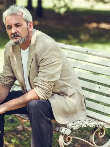 Bărbat cu părul grizonat, așezat pe o bancă în parc