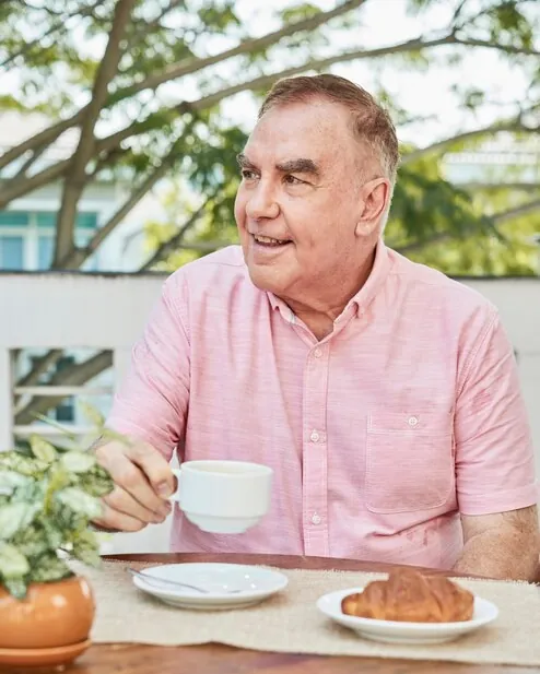 Bărbat în vârstă cu o cafea și un croasant la masa unei terase
